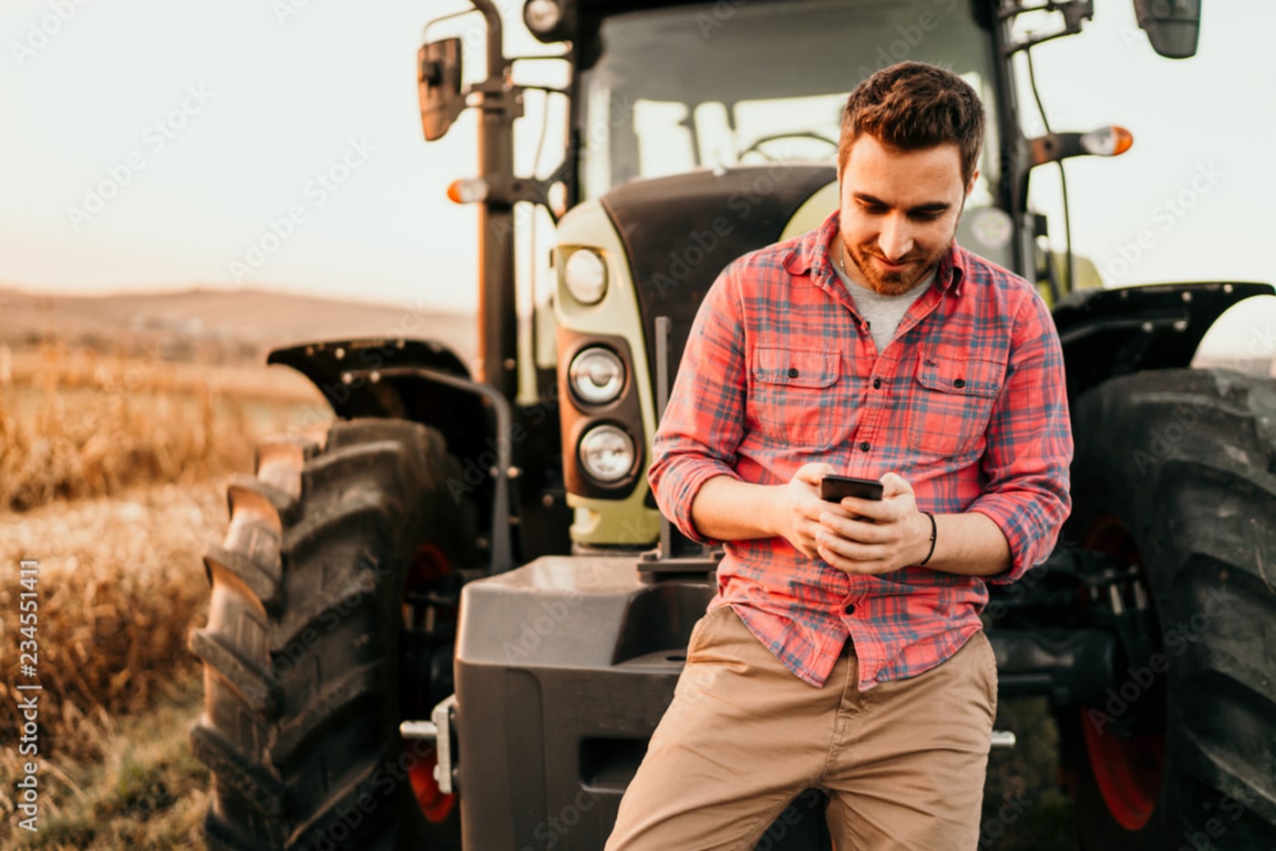  Man holding cell phone leaned up against a tractor in a field 